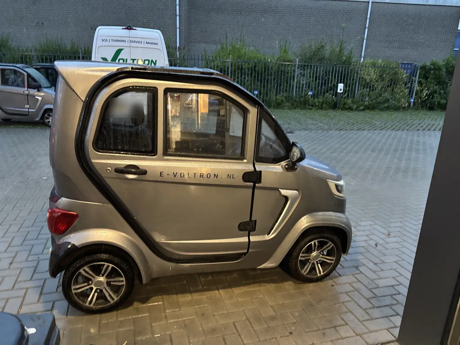 Grijze elektrische brommobiel met Voltron-belettering voor de servicebus bij de werkplaats in Weesp
